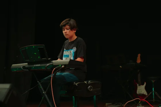 studiante de Musicarte concentrado tocando el teclado en una presentación en vivo, ejemplificando la disciplina de la práctica y el enfoque desarrollados en las clases de música.